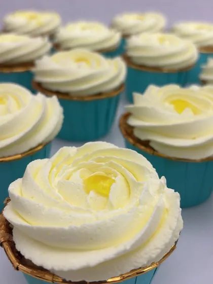 A close-up on a vanilla cupcake with a lemon filling, topped with a beautiful white frosting rose. The simple elegance makes it a classic choice.
