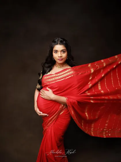 The vibrant red of this saree with its gold border creates a striking and powerful image. The flowing fabric adds a sense of movement and life to this beautiful maternity portrait.