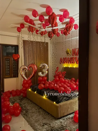 Here is another example of a full room anniversary surprise. I filled the space with red balloons, including a large heart-shaped foil balloon and a silver number '3' to celebrate their special day. The goal is to make the entire room feel like a celebration.