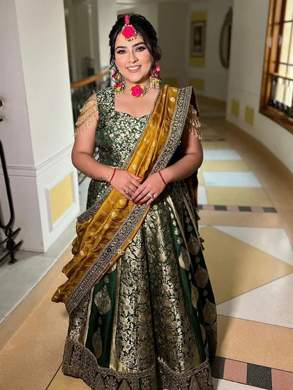 A full-length shot showcasing the bride's stunning Mehendi outfit and her radiant smile. She looks comfortable and happy, ready to get her henna done.