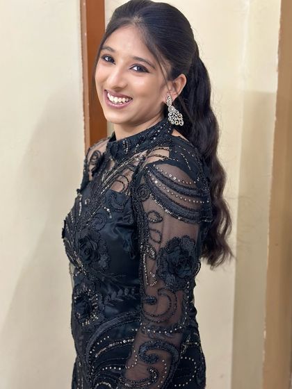 The joy of a great hair and makeup day. This client is all smiles, showing off her modern black ensemble paired with a sophisticated wavy ponytail and glowing makeup.