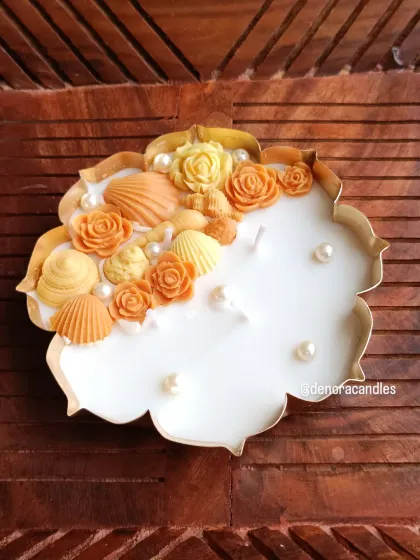 A unique urli candle design featuring seashell and rose wax figures in warm orange tones, accented with pearls.