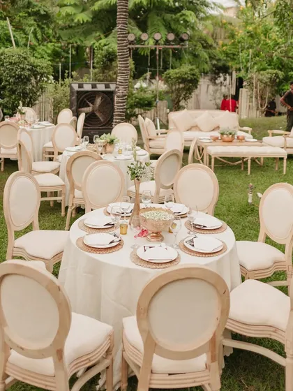 An elegant outdoor seating arrangement for a 75th birthday party. The neutral color palette of the chairs and tables, combined with the lush green lawn, creates a sophisticated and timeless garden party setting.