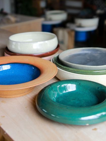 A stunning array of plates and shallow bowls with wide rims, showcasing the students' mastery over form and their exploration of vibrant, contrasting glazes.