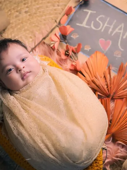 A beautiful overhead shot of a newborn wrapped snugly in a basket, personalized with a little chalkboard slate announcing her name, Ishanvi.