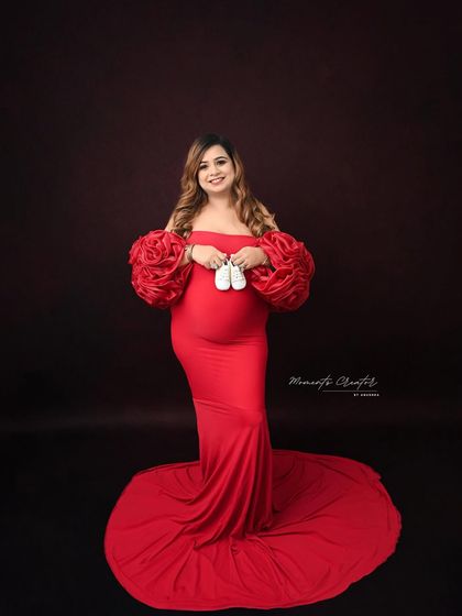 Holding tiny shoes, a sweet symbol of the little one to come. This classic solo portrait in a vibrant red gown is full of anticipation and joy.