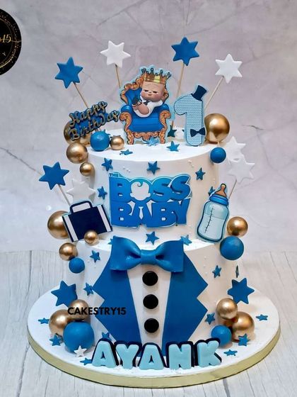 A powerful two-tier Boss Baby cake for a first birthday. This 5kg pineapple cake is decorated in blue, black, and gold, featuring the iconic suit, briefcase, and a custom nameplate.