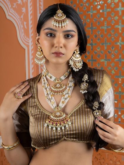 A full view of our heritage bridal look, featuring layered Kundan pearl necklaces, statement chandbali earrings, an ornate maang tikka, and intricate braid accessories. This ensemble celebrates the grandeur of traditional Indian craftsmanship.