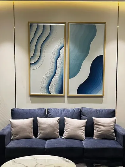A close-up of the seating arrangement in the Noida project, showing the interplay of colors and textures. The deep blue sofa is paired with neutral cushions, and the abstract wall art ties the color scheme together, creating a harmonious and visually engaging living area.