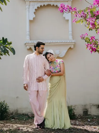 A romantic portrait of the couple at their Welcome Lunch. The groom's pastel pink embroidered jacket and the bride's sage green floral saree create a soft, coordinated, and elegant look.
