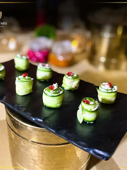 These cucumber roll-ups are a light and refreshing appetizer option. Thinly sliced cucumber is wrapped around a creamy filling and garnished with pomegranate seeds, served on a black slate platter for a modern look.