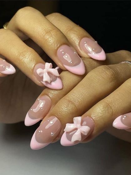 A soft and sweet design with a pink French tip, pearl accents, and 3D bows. This is a perfect example of the popular 'coquette' nail trend.