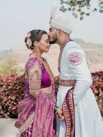 A tender moment between the bride and groom. The groom's kiss on her forehead captures the love, while her intricate blouse and hairstyle showcase the detailed styling.