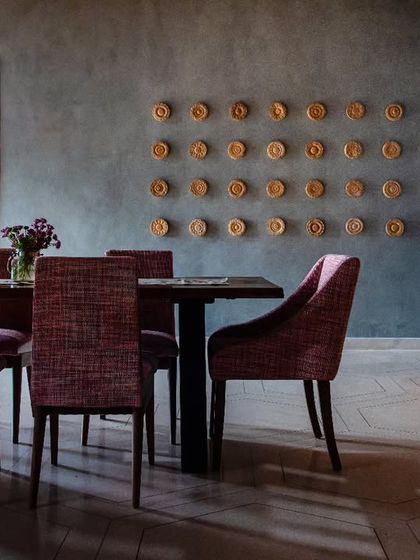 The dining lounge at Anthea Pharma, where earthy-toned fabrics add a pop of color against the raw, textured backdrop. Delicately carved circular artwork contrasts beautifully with the rustic concrete wall.