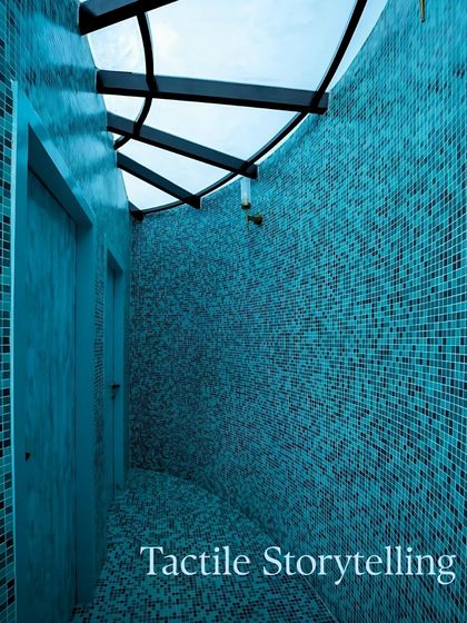 A detail shot of the curved mosaic-tiled bathroom, emphasizing the tactile quality of the tiles and the way the skylight above creates a dynamic interplay of light and shadow.