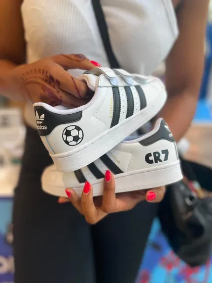 For the football fans. A customer holding up a pair of Adidas Superstars we customized with a CR7 and soccer ball theme. We can tailor designs to any passion, making it a perfect fit for sports-related events.