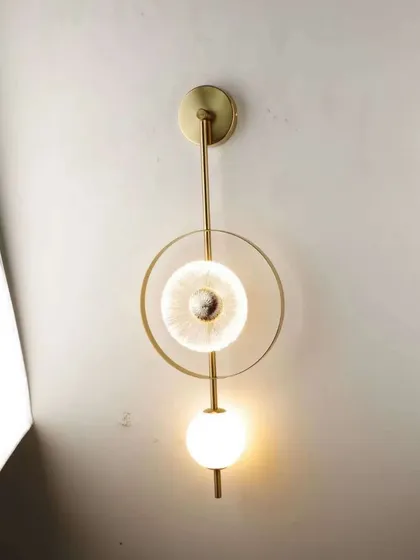 A modern wall sconce featuring a mix of geometric shapes, including a textured glass disc and a frosted globe.