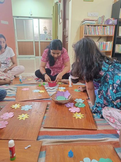 The storyteller helps distribute materials for the craft, ensuring everyone has what they need to get started.