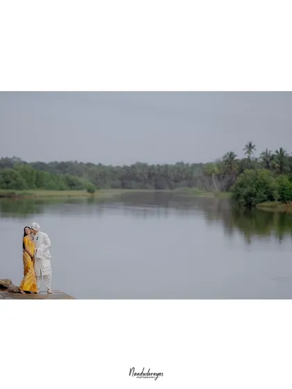 A wide, panoramic shot of a couple standing by the river, emphasizing the vastness of the landscape and the intimacy of their moment.