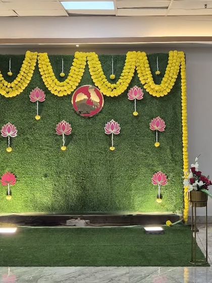 A beautiful baby shower backdrop with an artificial green wall, marigold garlands, and lotus flower hangings.