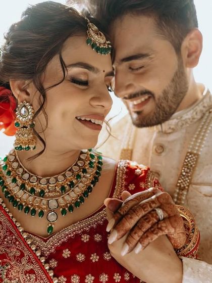 A close-up of the couple, their smiles radiating happiness, with the bride's stunning green jewelry in focus.