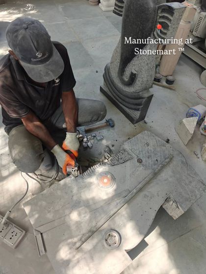 An artisan at work on a large granite Ganesha sculpture, with a finished piece in the background. This shows our capacity to produce multiple large-scale sculptures.