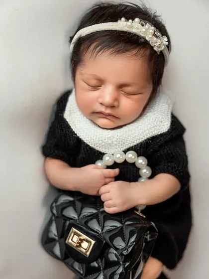 The final portrait from our little fashionista session. The baby is dressed in a classic black-and-white knit outfit, holding a string of pearls and a tiny handbag.