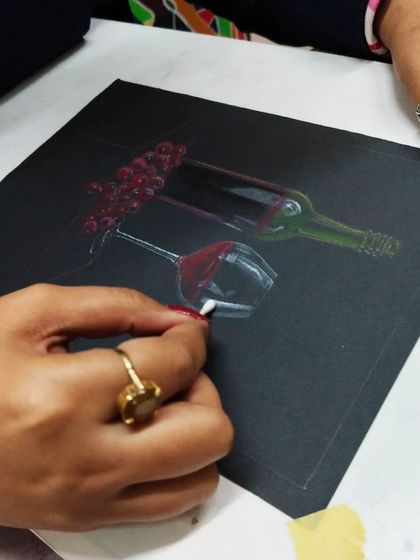 A close-up of a student using oil pastels on black paper to create a still life of a wine bottle and glass, a technique that makes colors pop.