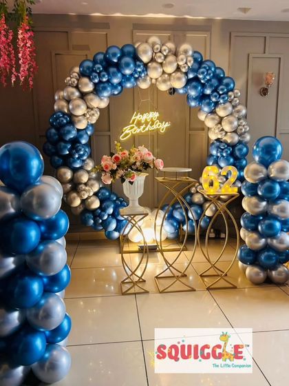 A chic birthday setup with a blue and silver chrome balloon arch and a 'Happy Birthday' neon sign.