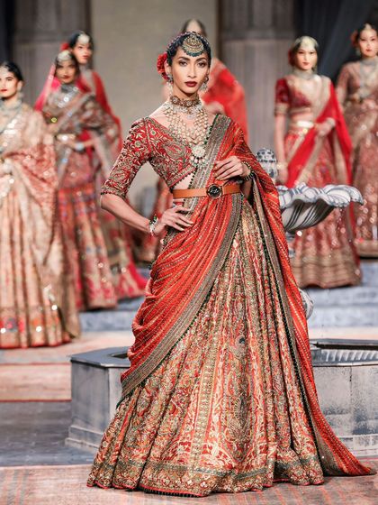 A powerful runway pose, this image captures the model in a striking red lehenga, commanding attention at the center of the stage.