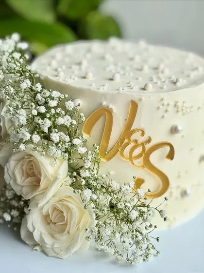 This angle showcases the depth of the floral arrangement and the shimmer of the gold topper against the pristine white buttercream.