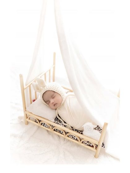 Sweet dreams in a tiny bed. A swaddled newborn with a bunny hat sleeps on a miniature wooden bed, creating an incredibly cute and gentle portrait that highlights how small and precious they are.