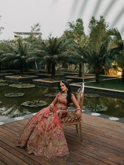 A regal portrait of the bride seated on an ornate chair by the water. Her pose is confident and elegant, perfectly capturing the grandeur of her Udaipur wedding.