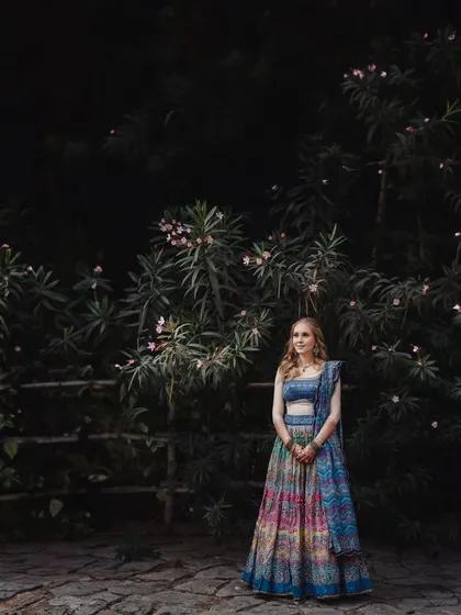 A stunning bridal portrait against a dark, moody backdrop of trees. The contrast makes the bride's colorful lehenga stand out beautifully.