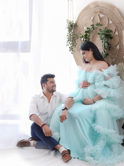 A tender moment between partners. The dad-to-be sits at his partner's feet as she sits enthroned in a stunning light blue gown, a picture of serene love.
