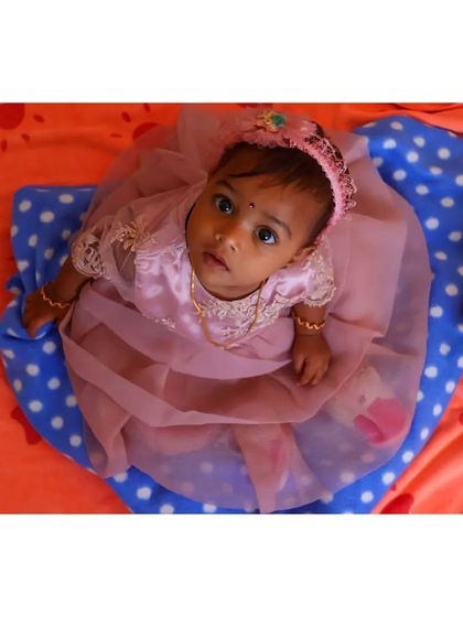 An overhead shot of a baby girl in a lovely pink dress, looking up with wide, curious eyes. This perspective creates a unique and engaging portrait.