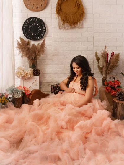 A dreamy solo portrait in our boho-chic studio corner. The mom-to-be is surrounded by a sea of soft peach ruffles from her gown, creating a whimsical and ethereal look.