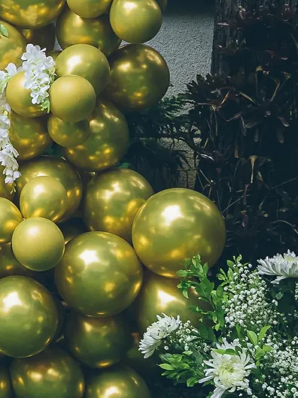 The contrast of metallic gold balloons against dark foliage and fresh white flowers creates a dramatic and beautiful effect. This is an example of how I use color and texture to create high-impact decor.