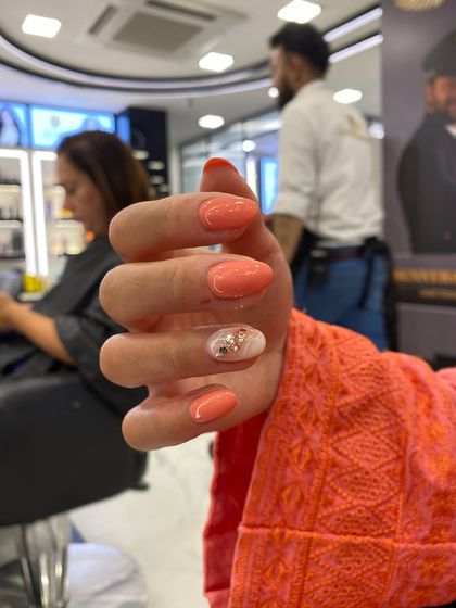 A peachy-coral set with a single accent nail featuring inbuilt glitter and stones for a touch of sparkle.