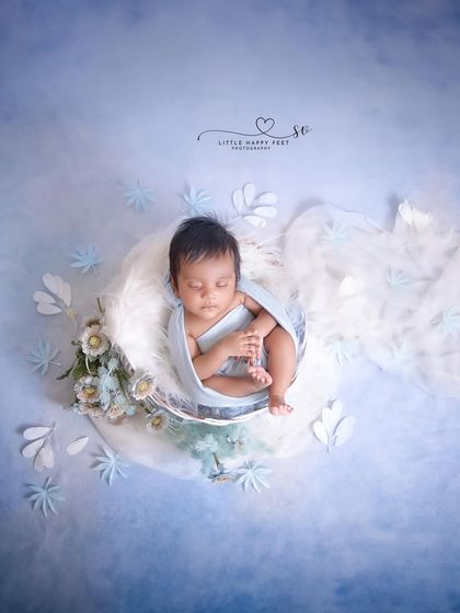 Cradled in warmth. This overhead shot of a baby wrapped in blue, surrounded by white flowers, is a beautifully composed and serene portrait.