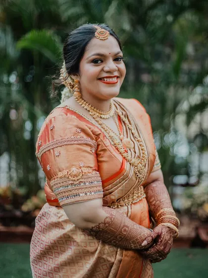 A beautiful outdoor portrait of a South Indian bride. The natural lighting enhances her glowing skin, and the makeup is kept classic to complement her traditional attire.