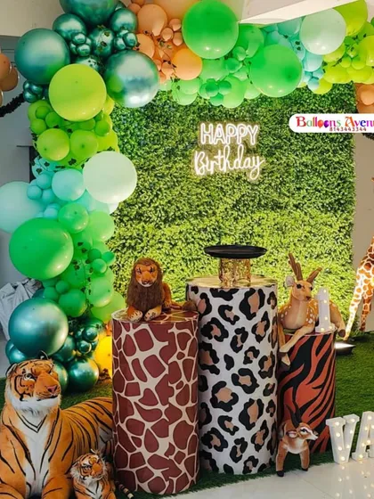 We used a lush green wall as the backdrop for this jungle-themed first birthday. The decor includes an organic balloon arch, animal-print plinths for the cake, large animal props, and illuminated letters for the birthday boy's name.