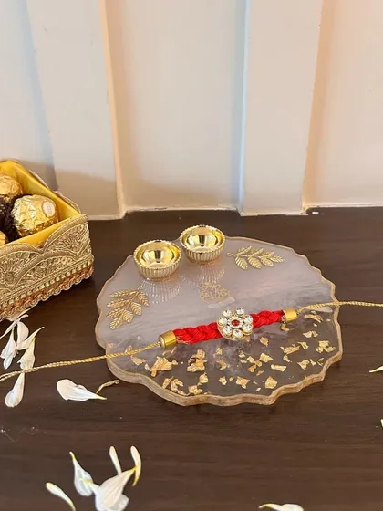 A beautiful resin thaali with a red rakhi, perfect for the ceremony. The gold leaf detailing on the thaali adds a touch of luxury to this traditional essential.