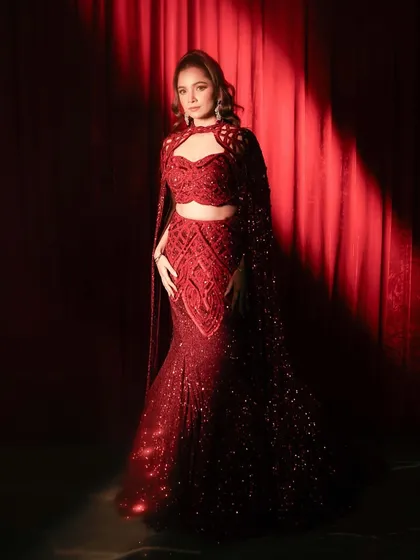 A client shines in a ruby red embellished lehenga with floor-sweeping sleeves and signature cutwork embroidery, a silhouette that moves with grace.