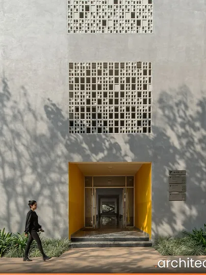 The entrance to Vidyashilp Academy, a UNESCO Happy School, is marked by a bright yellow portal set within a facade of concrete and 'jaali' screens. The design is functional and eco-conscious, creating an enriching experience for students.