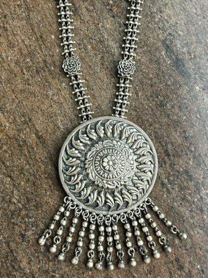A statement oxidised silver pendant with a sunburst design. The intricate metalwork and dangling ghungroos make this a truly special piece.