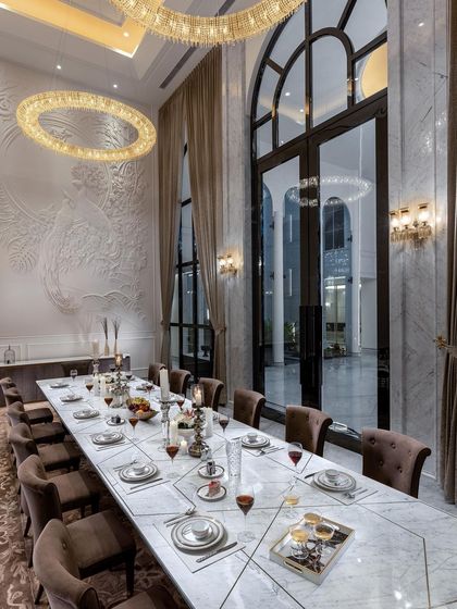 The formal dining room in The Grand Alabaster is designed for grand entertaining. A long marble table sits beneath a dramatic ring chandelier, with double-height arched windows providing a view of the courtyard and filling the space with an air of majesty.