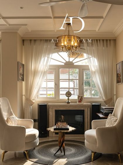 A wider view of the vintage-inspired seating area, complete with a fireplace, elegant chandelier, and an arched window that fills the room with light.