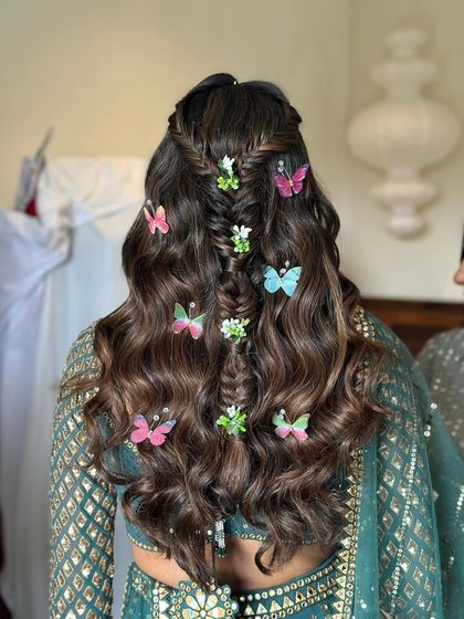 A creative mehndi hairstyle featuring a fishtail braid down the center, flanked by soft waves. I added colorful butterfly and floral accessories for a whimsical, garden-party feel.