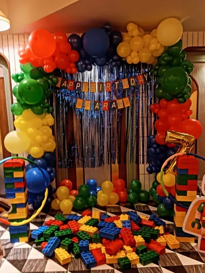 A fun and interactive Lego-themed birthday party. The decoration includes columns made of Lego-like blocks, a colorful balloon arch, and a pile of large blocks for kids to play with.